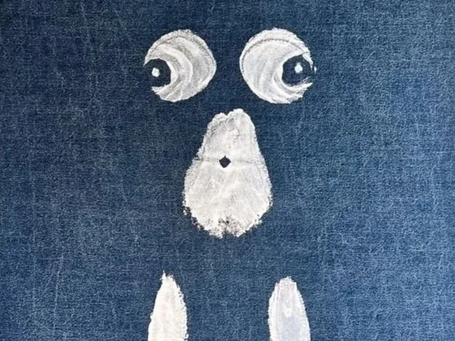 Close-up of a body paint in white on blue fabric, with two eyes, a nose, and a mouth.