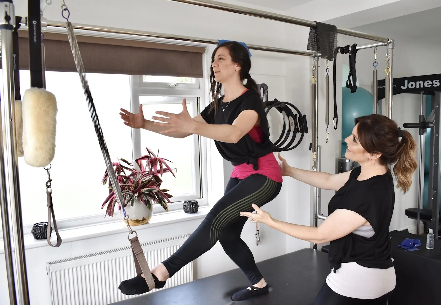 Woman receiving assistance from an instructor while practicing a Pilates exercise using a reformer in a fitness studio.