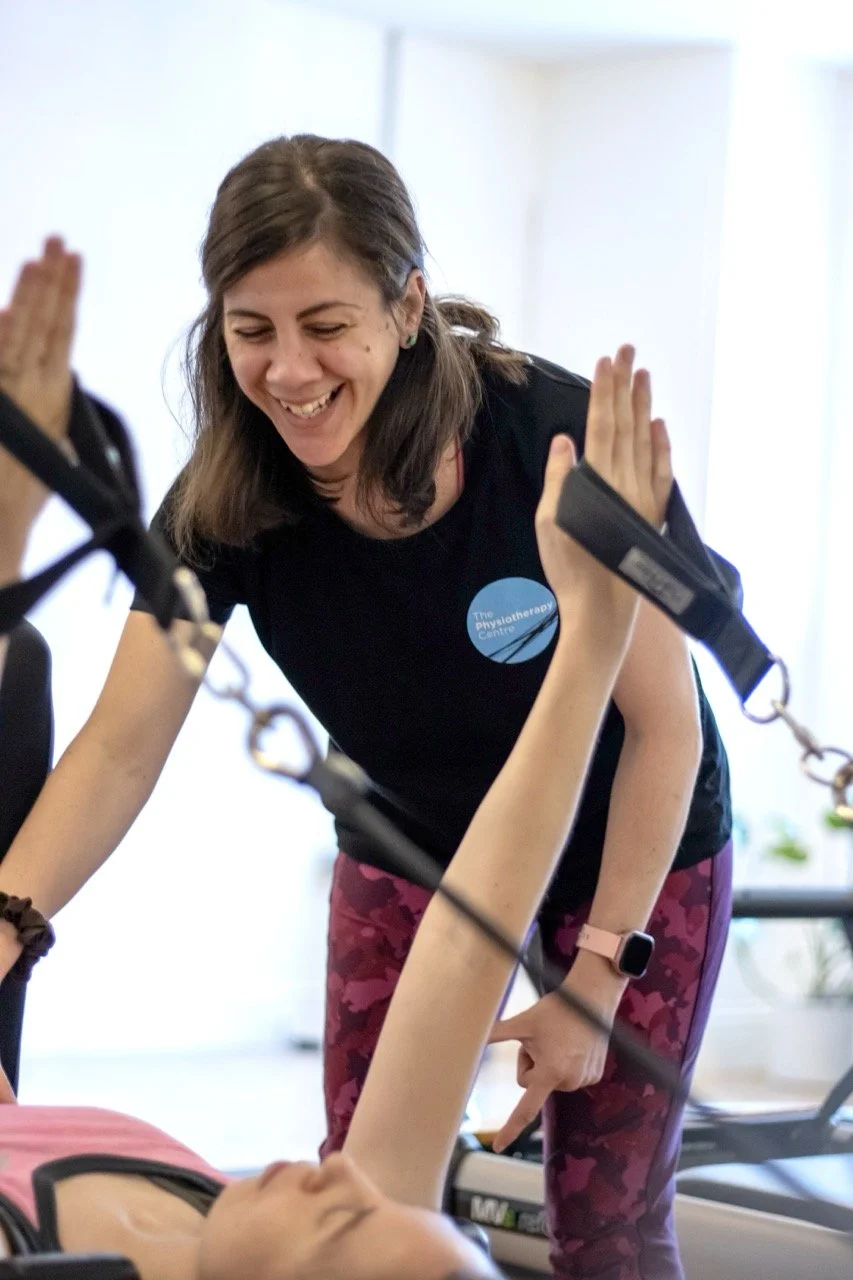 Female physiotherapist smiles whilst helping a client with a pilates reformer stretch on the reformer equipment.