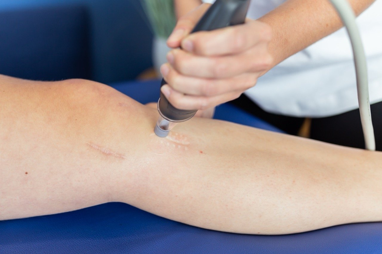 A person receiving a lympatouch therapy treatment on their lower leg, with visible scars.