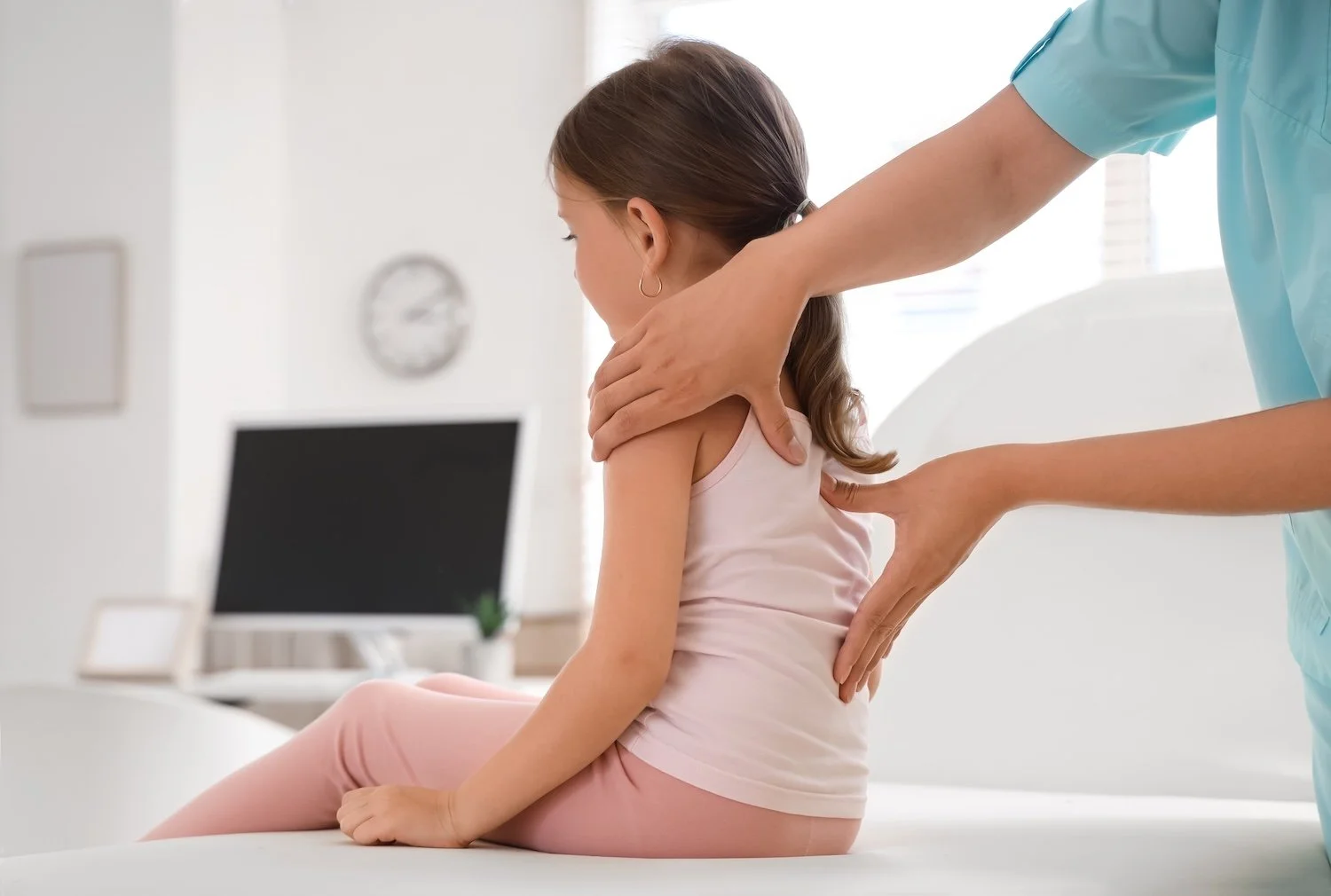 A physiotherapist examining a young girl by touching her shoulder and stomach in a clinic setting.