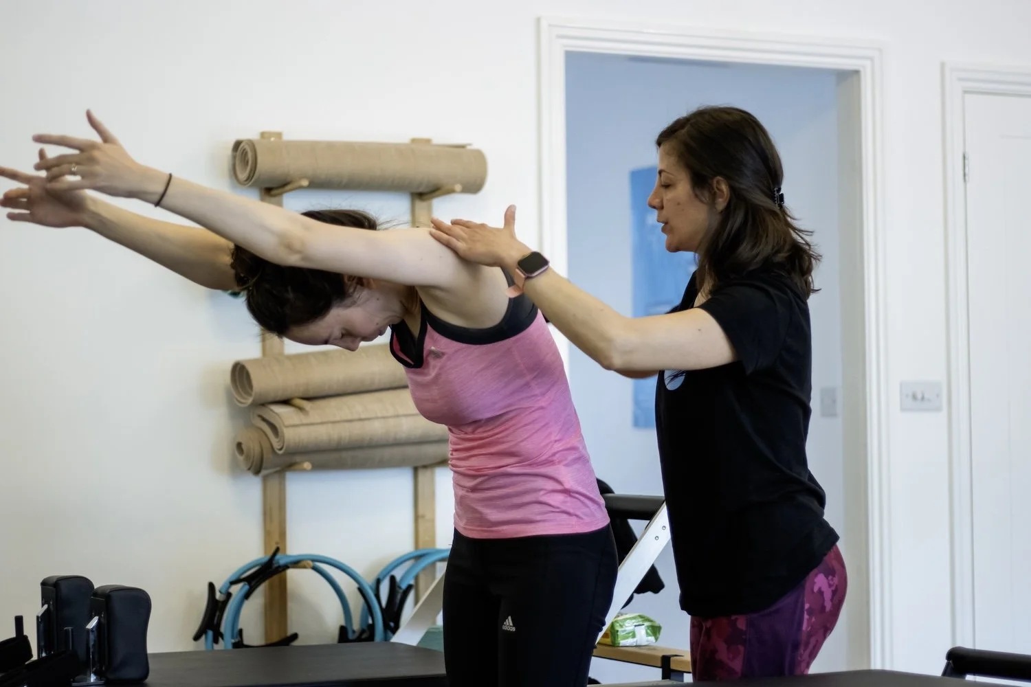 Female physiotherapist in a black t-shirt and purple marbled leggings stretching out a patients back in a physio clinic.