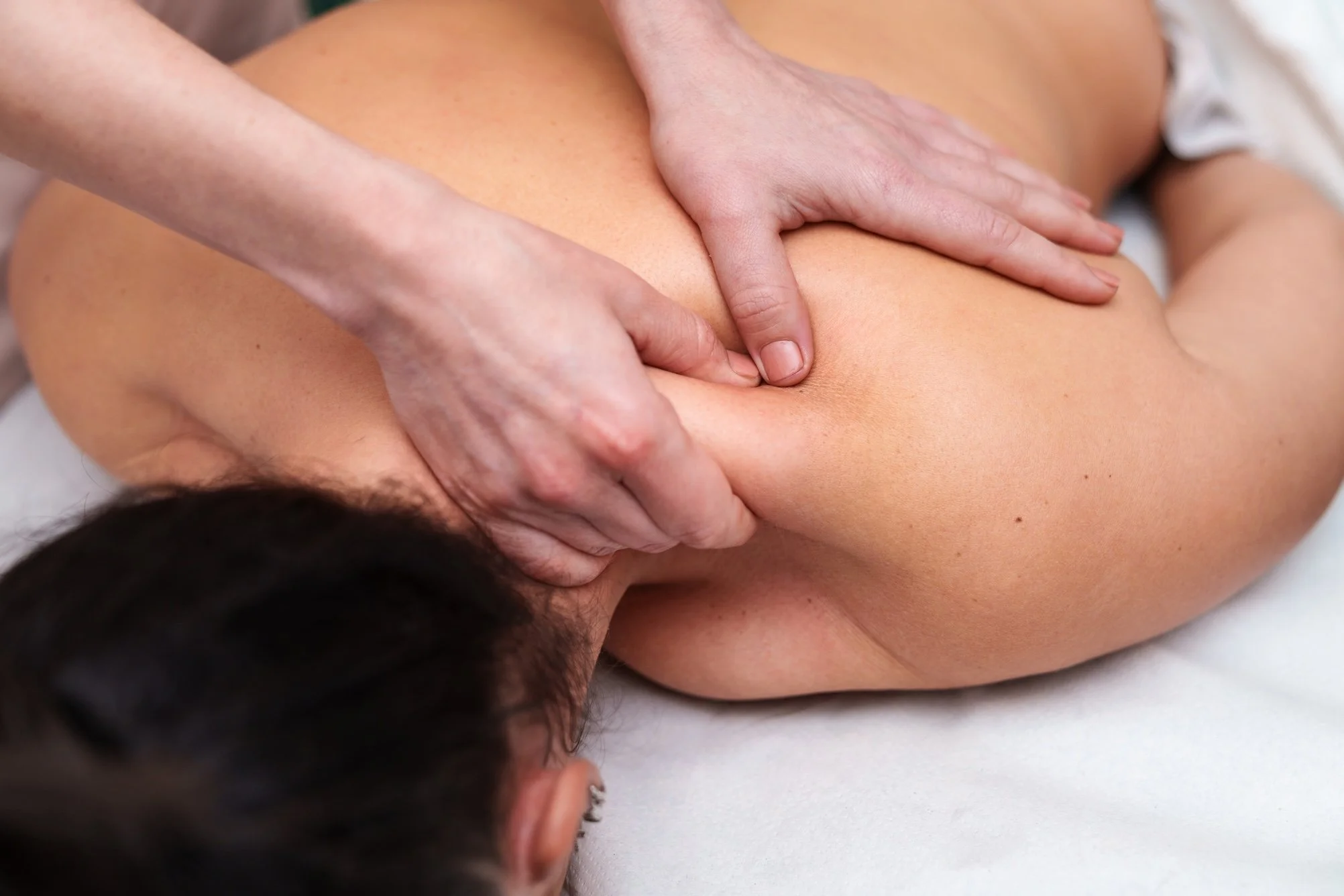 A person receiving a massage on their back, with hands applying pressure on the shoulder area.