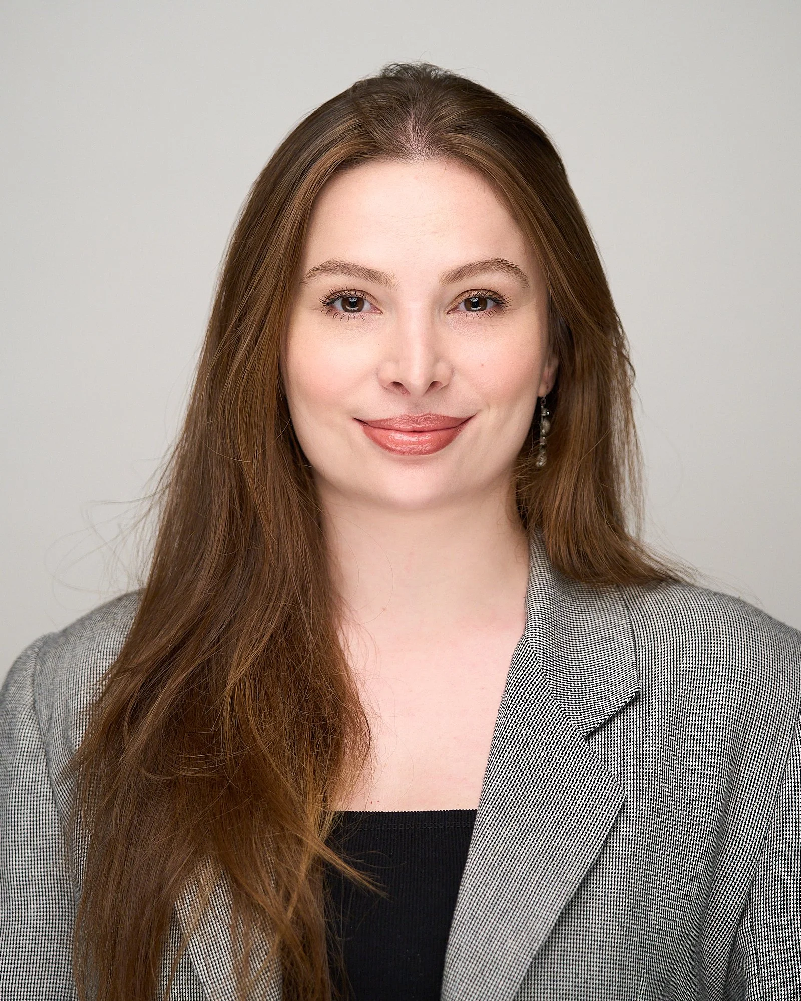 Mulher com cabelo castanho, usando blazer xadrez, sorrindo, fundo neutro.