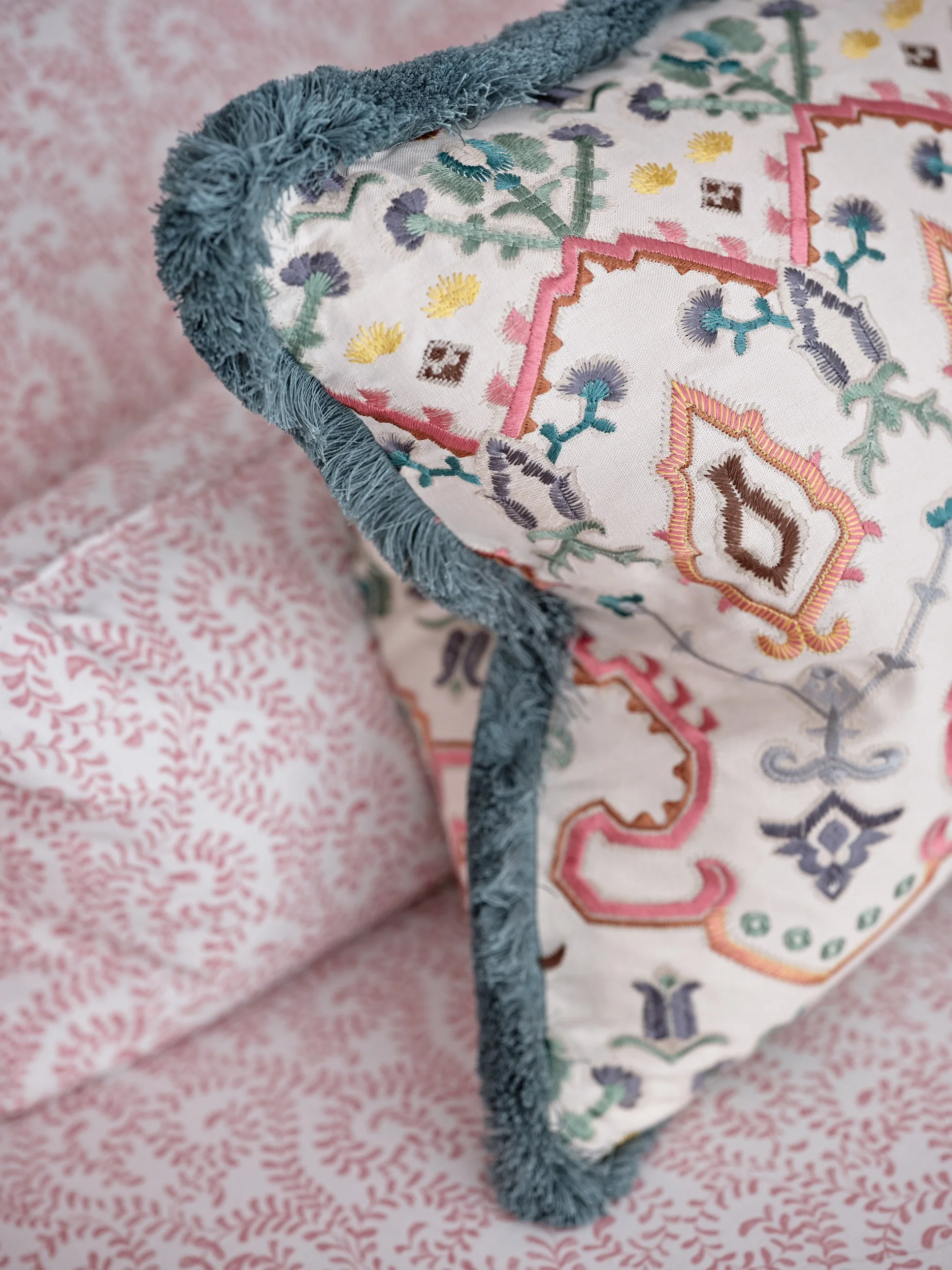 Close-up of embroidered fabric with floral patterns and a blue, fuzzy trim.