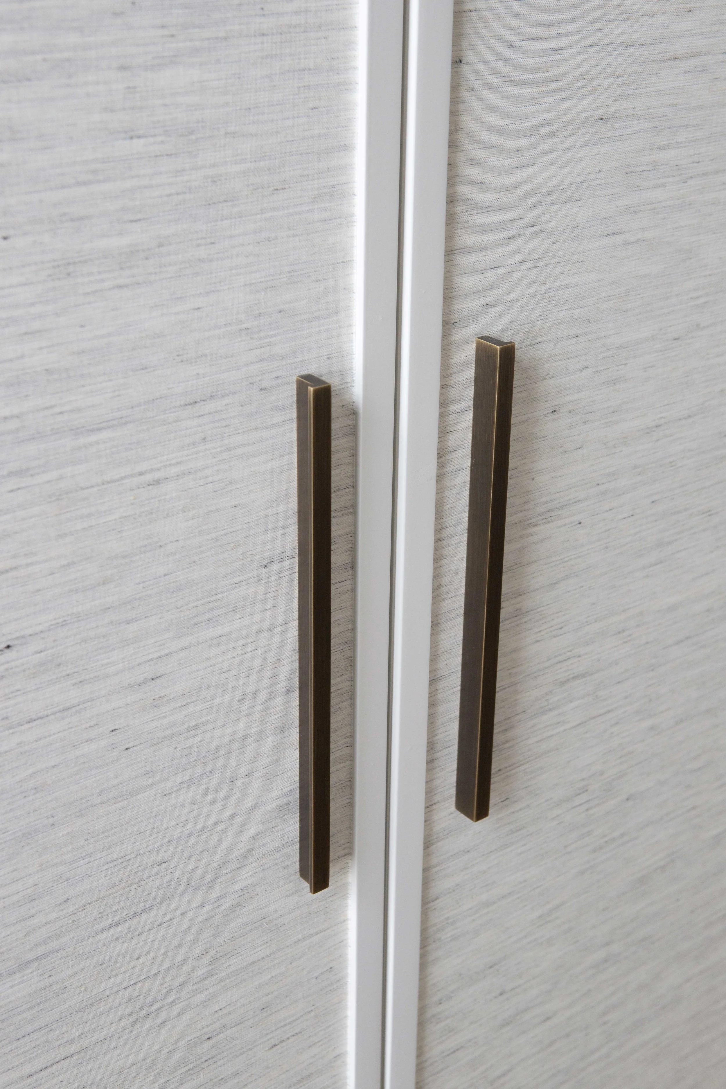 Close-up of two cabinet doors with vertical bronze handles, against a beige textured wall.