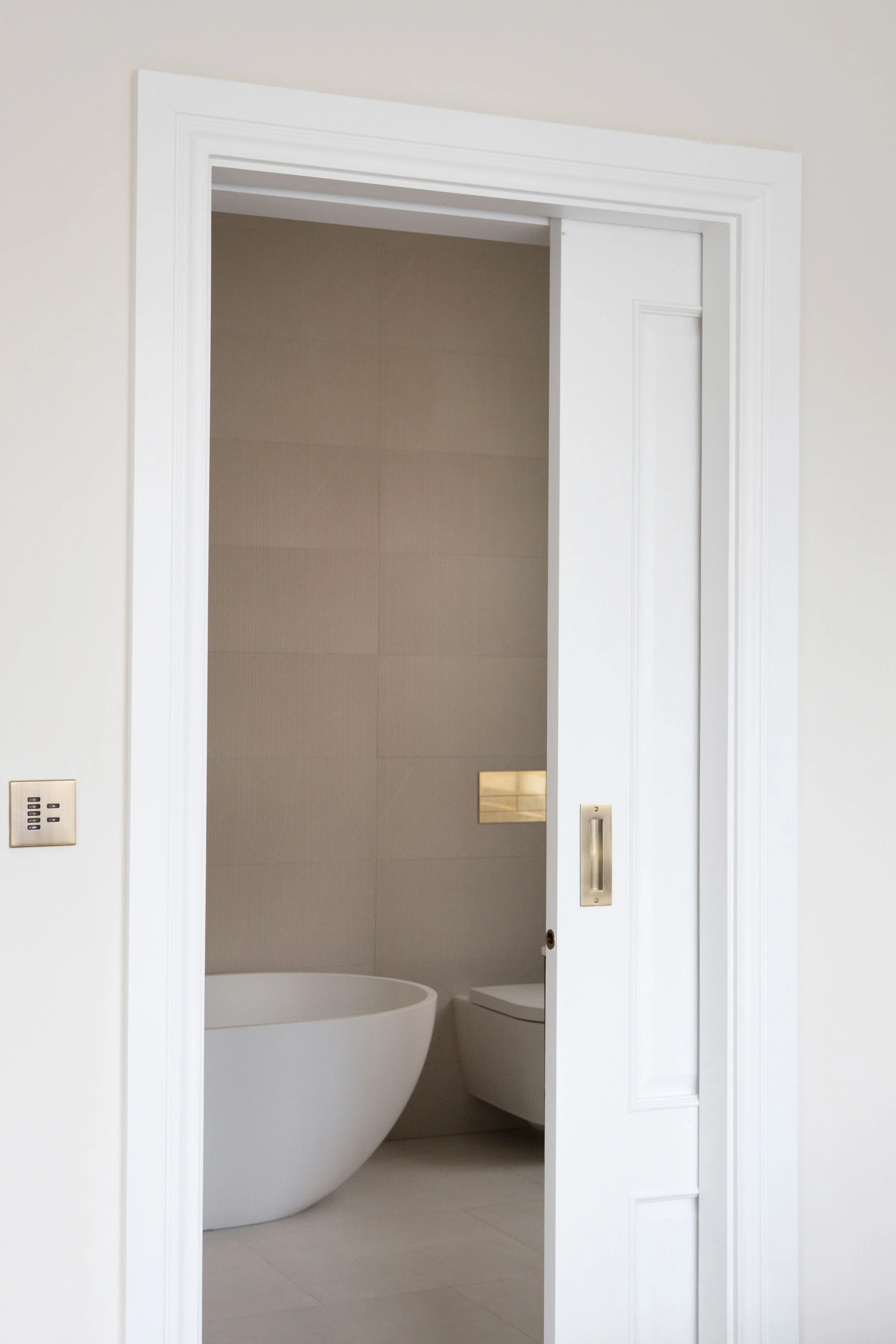 Interior of a bathroom with a freestanding bathtub, a toilet, and tiled walls seen through a doorway with white trim.