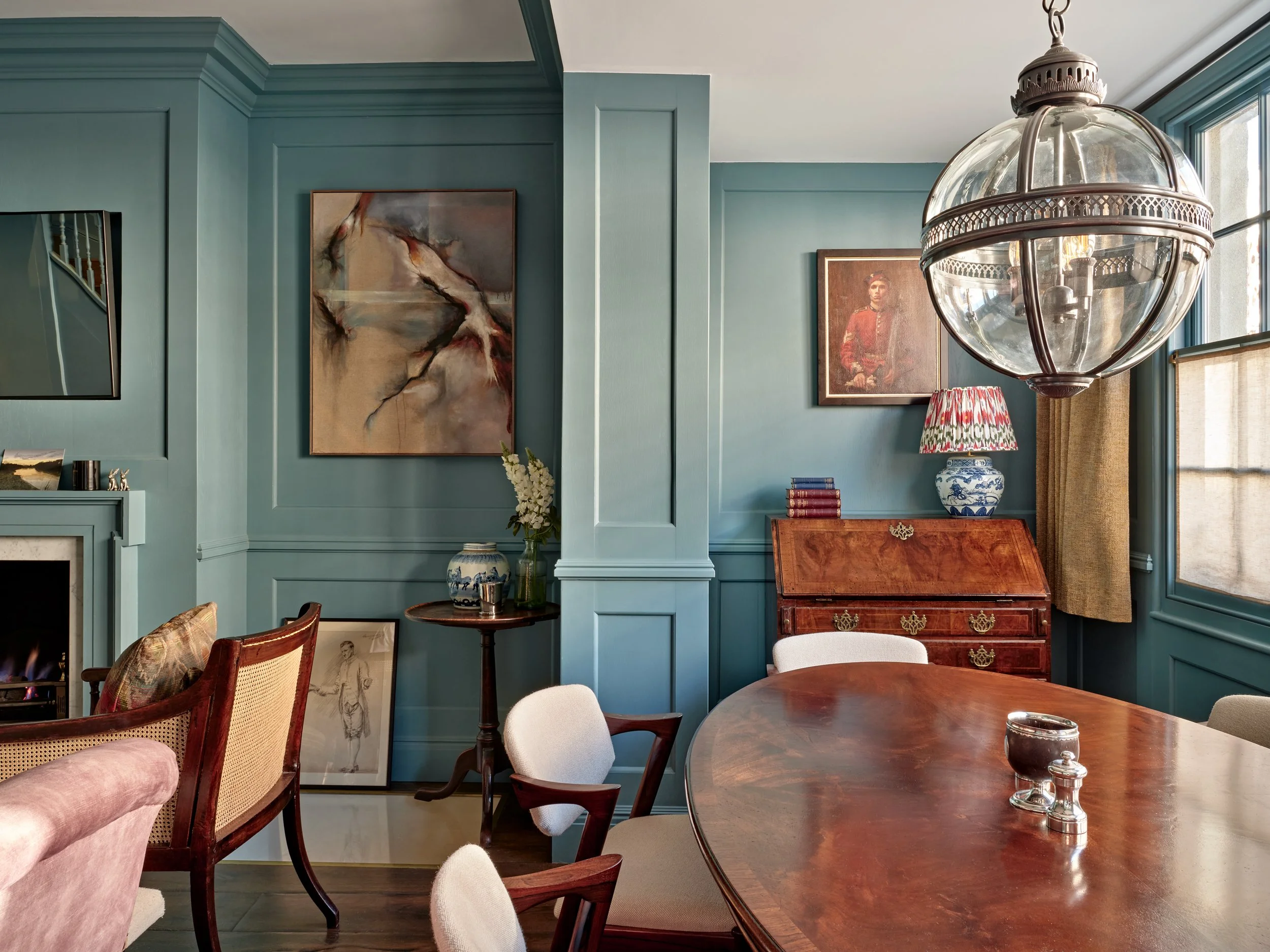 Interior of a room with teal walls, large window, and various artworks, including a large abstract painting and a portrait of a woman, along with furniture and decorative items.