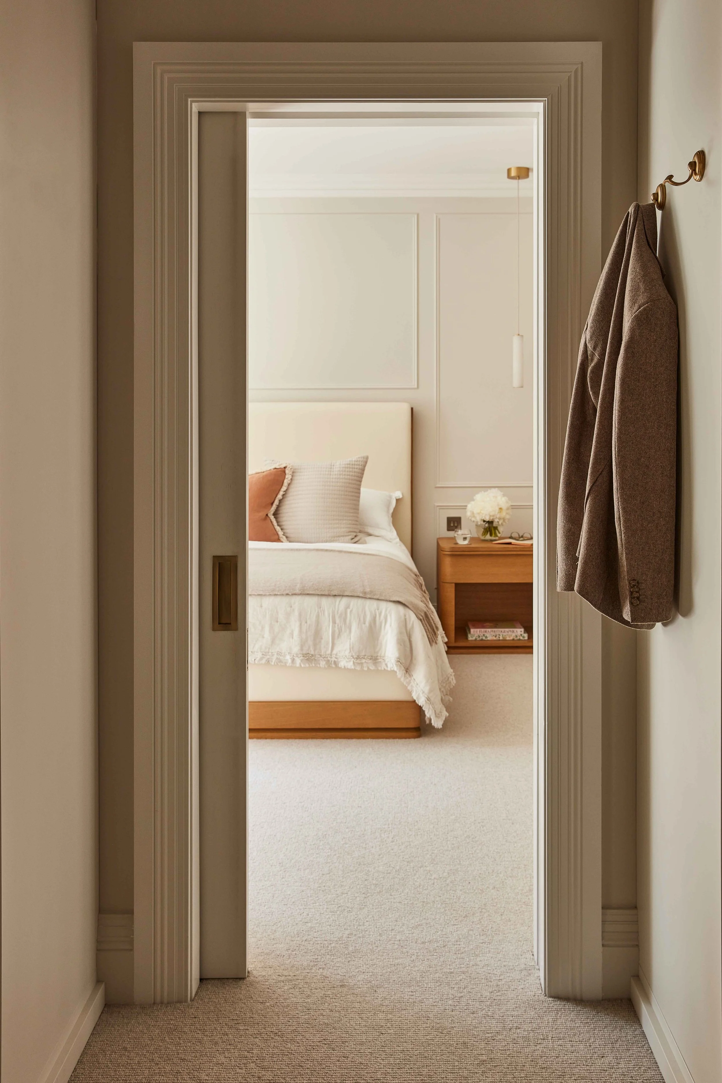 A view through a doorway into a bedroom with a bed, pillows, and a nightstand with flowers.