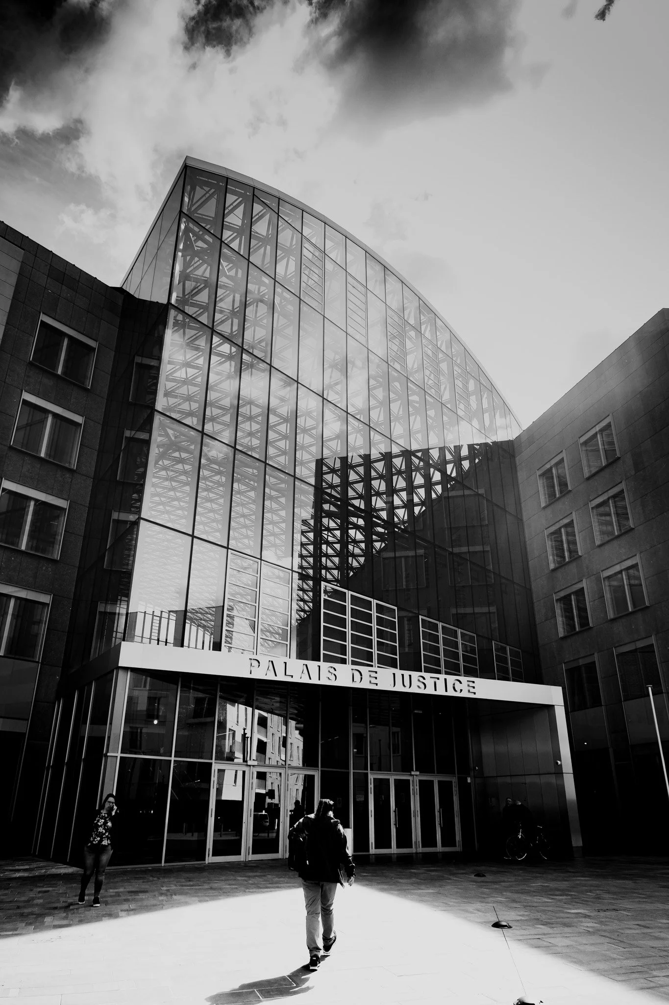 Vue en noir et blanc du bâtiment du Palais de Justice avec des personnes marchant à l'entrée.