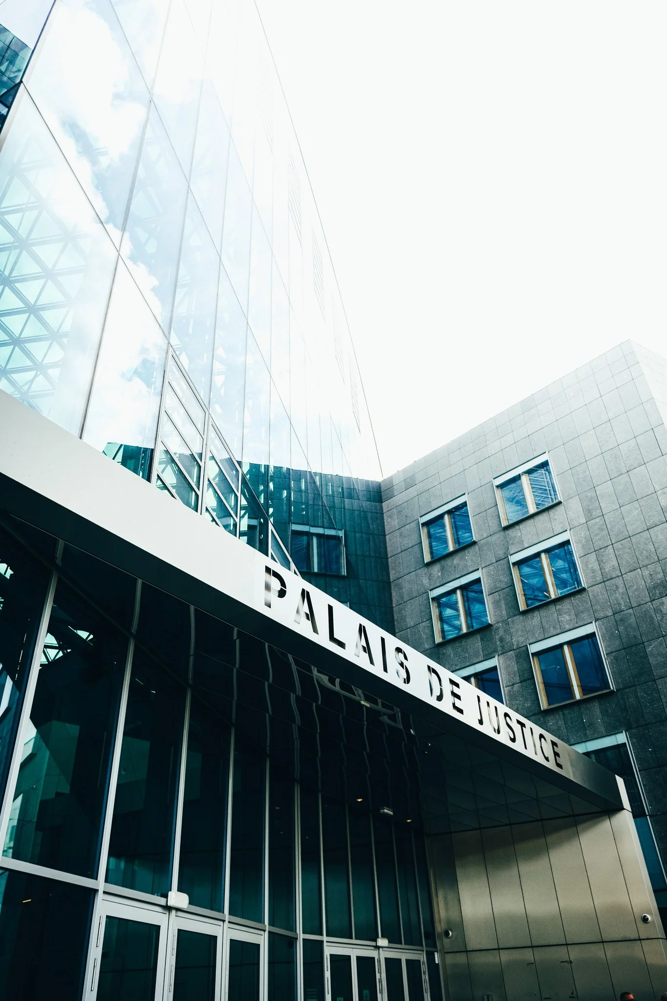 Façade en verre du Palais de Justice avec un panneau indiquant son nom.