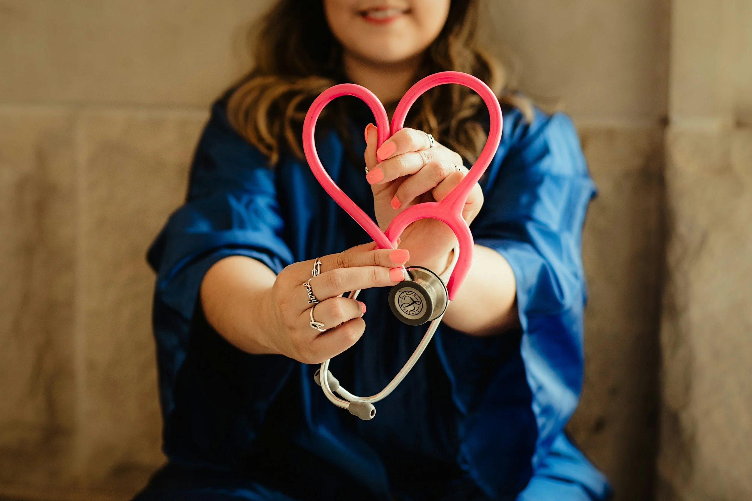 A woman holding a pink heart-shaped stethoscope.
