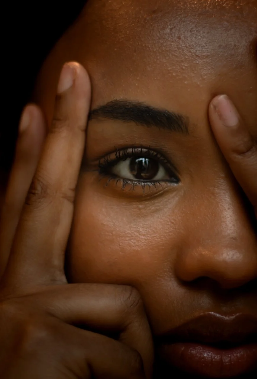 Close-up of a person with dark skin, holding their face with fingers, showcasing one eye and part of their face. Headshot. Portrait.