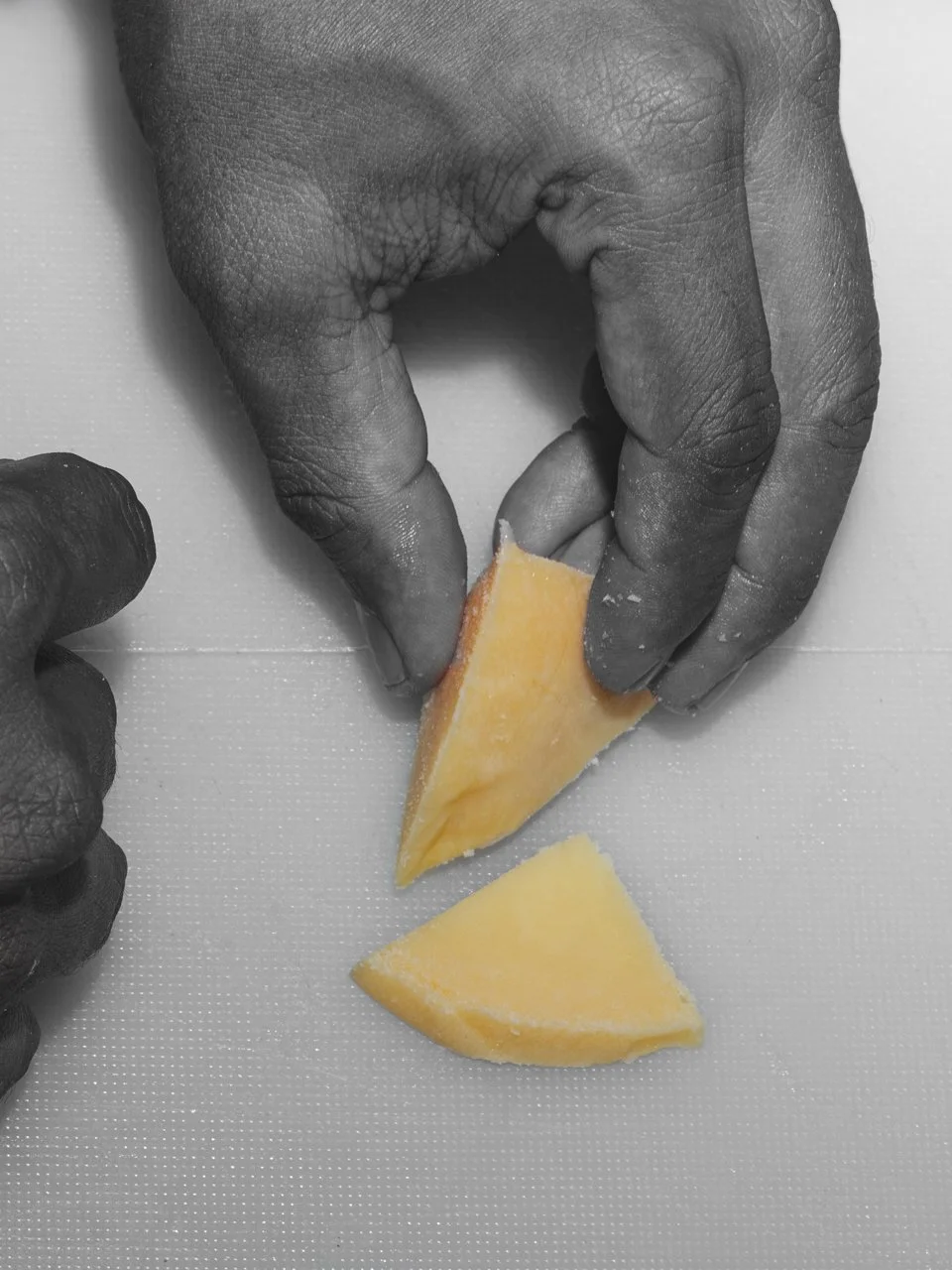 Hands chopping cheese on a cutting board.