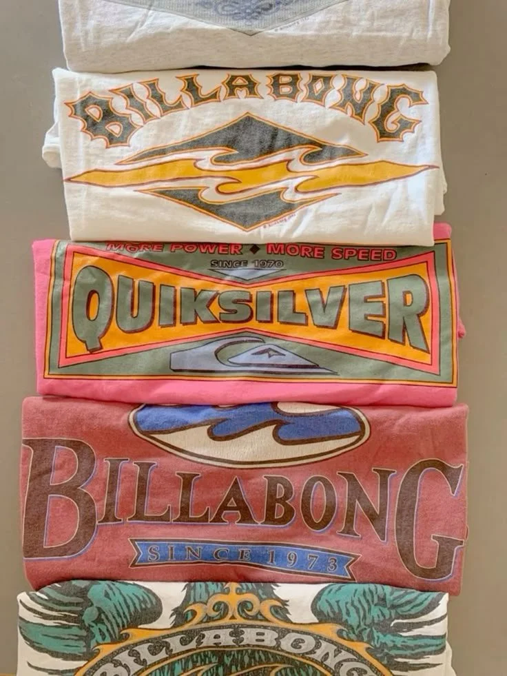 Stack of folded T-shirts with various surf and skate brand logos, including Billabong, Quiksilver, and others.