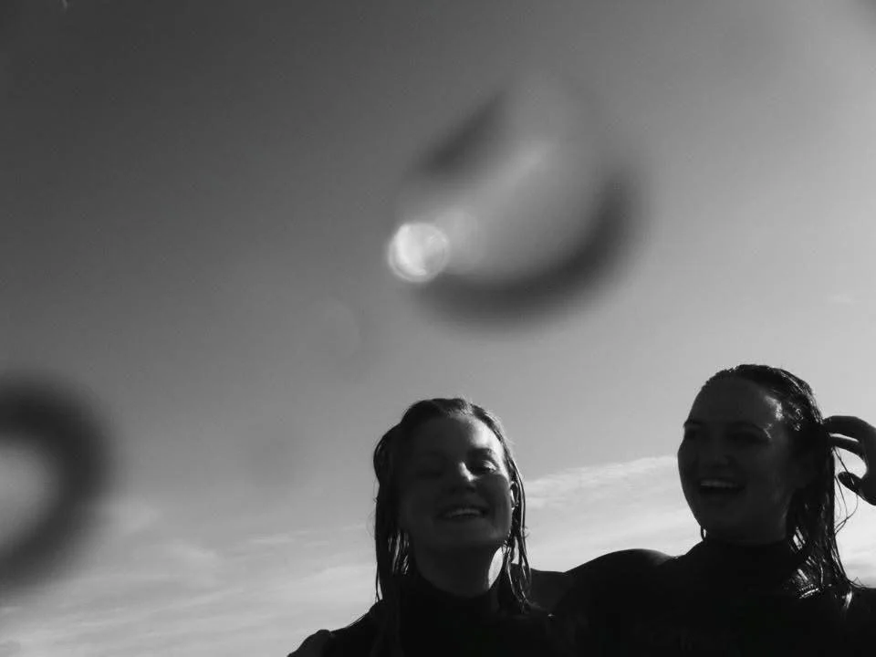 Two smiling women with wet hair outdoors, with a moon visible in the sky