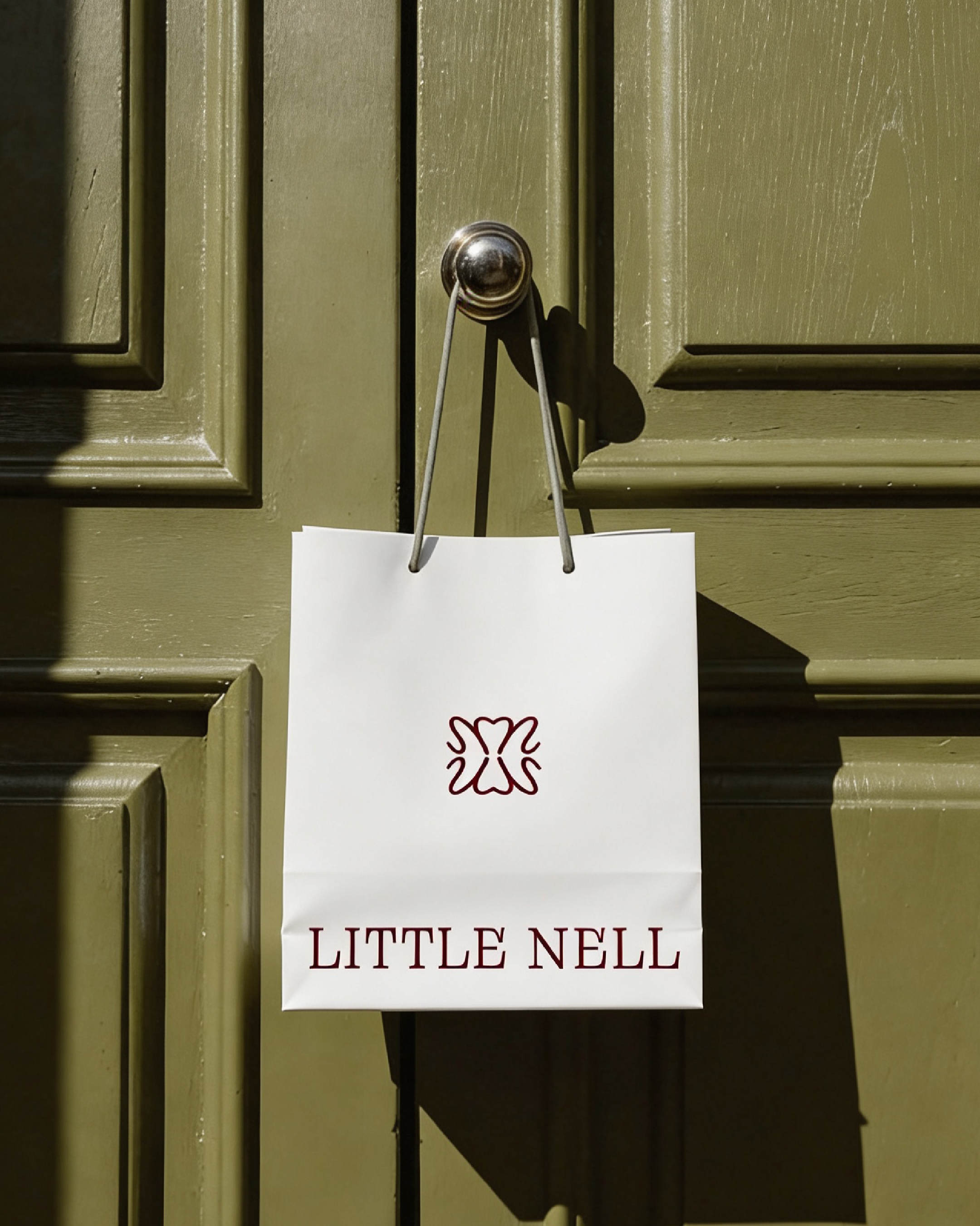 A green door with a shiny round silver doorknob and a white sign hanging from the doorknob with a drawing of a bird and the words 'LITTLE NELL' in red letters at the bottom.