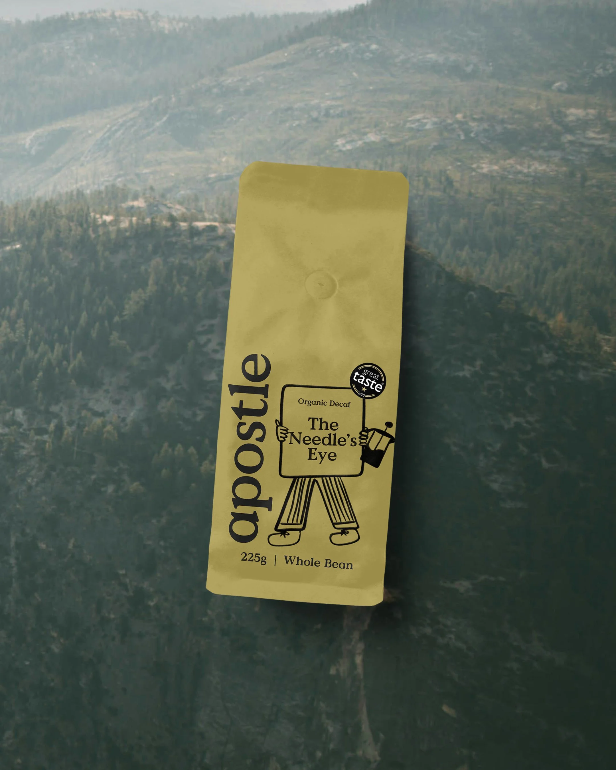 A yellow packaged food item labeled 'The Needle's Eye' with a cartoon illustration of a person holding a needle and a spools of thread. The package states it contains 225 grams of whole bean organic decaffeinated coffee and has a sticker that says 'g