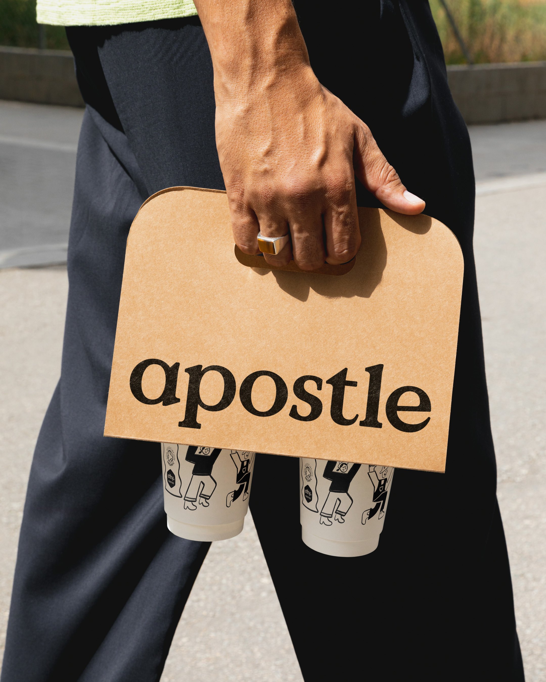 Person holding a brown paper bag and a cardboard envelope, standing outdoors.