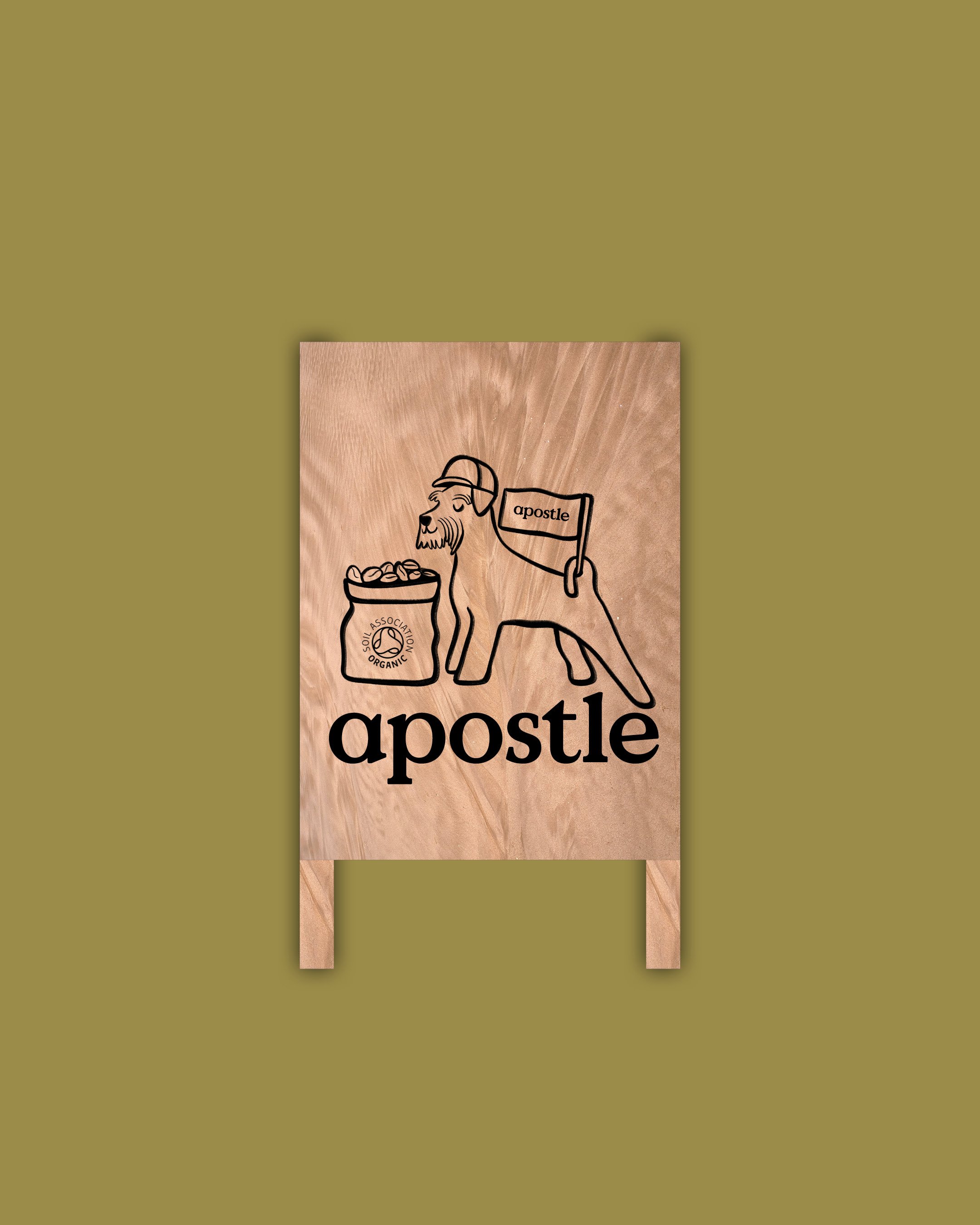 A wooden sign with a drawing of a lion wearing a cap and holding a bag labeled 'Soil Organic' and 'Apostle' with wooden stakes at the bottom, placed on a green background.