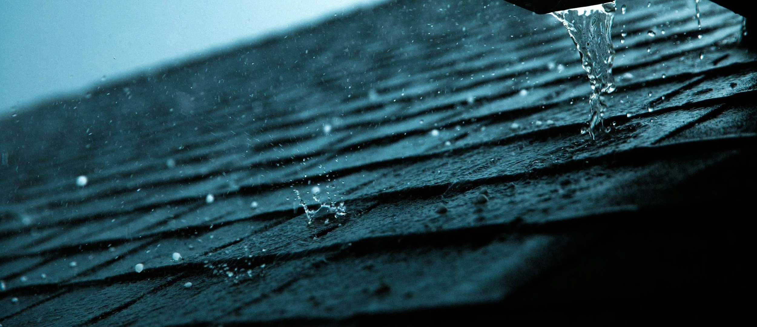 Close-up of water droplets falling onto a textured surface, possibly a black rubber mat, with water splashing.