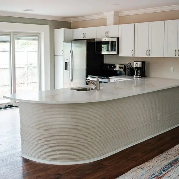 Kitchen with white cabinets, stainless steel appliances, and a curved white countertop island with a sink.