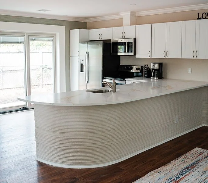Kitchen with white cabinets, stainless steel fridge, microwave, oven, coffee maker, and a curved white marble island with a sink.