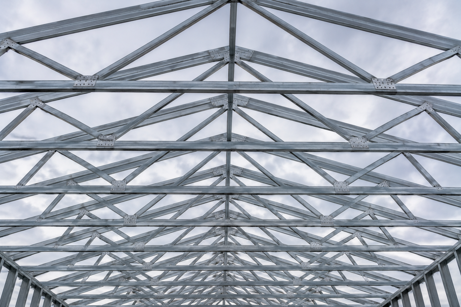 Metal framework of a building under construction with a cloudy sky background.