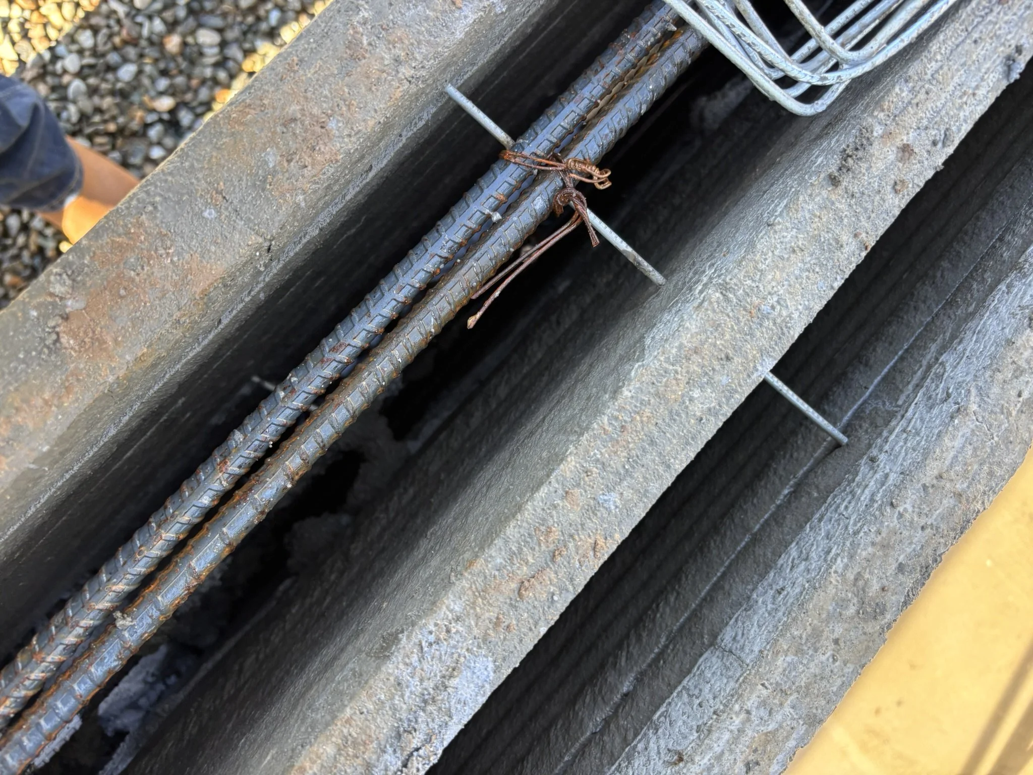 Close-up of steel rebar and wire ties in a concrete construction, with part of a yellow-painted edge visible.
