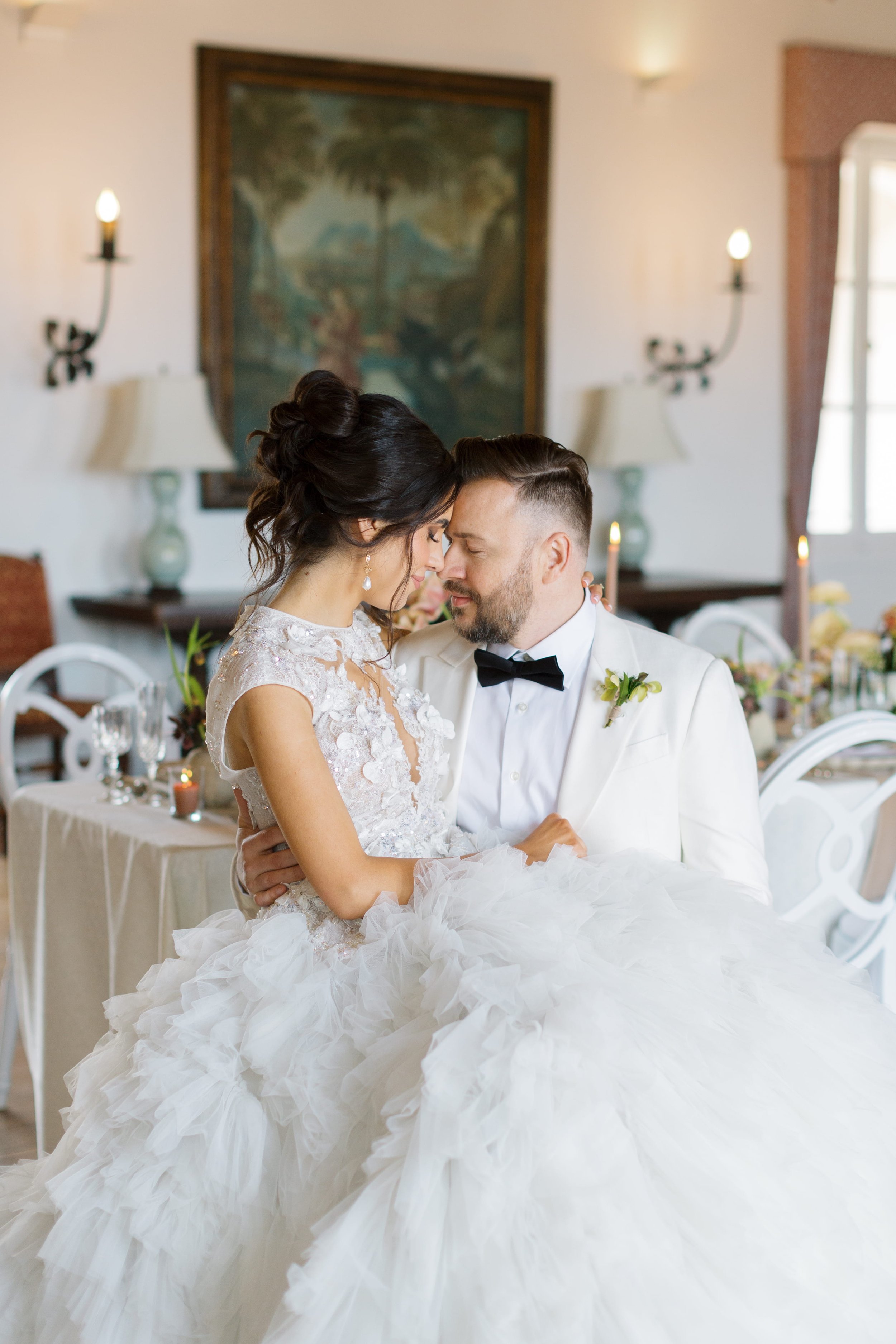 A bride and groom sharing an intimate moment at their wedding reception, smiling with their foreheads touching, in an elegant decorated room.
