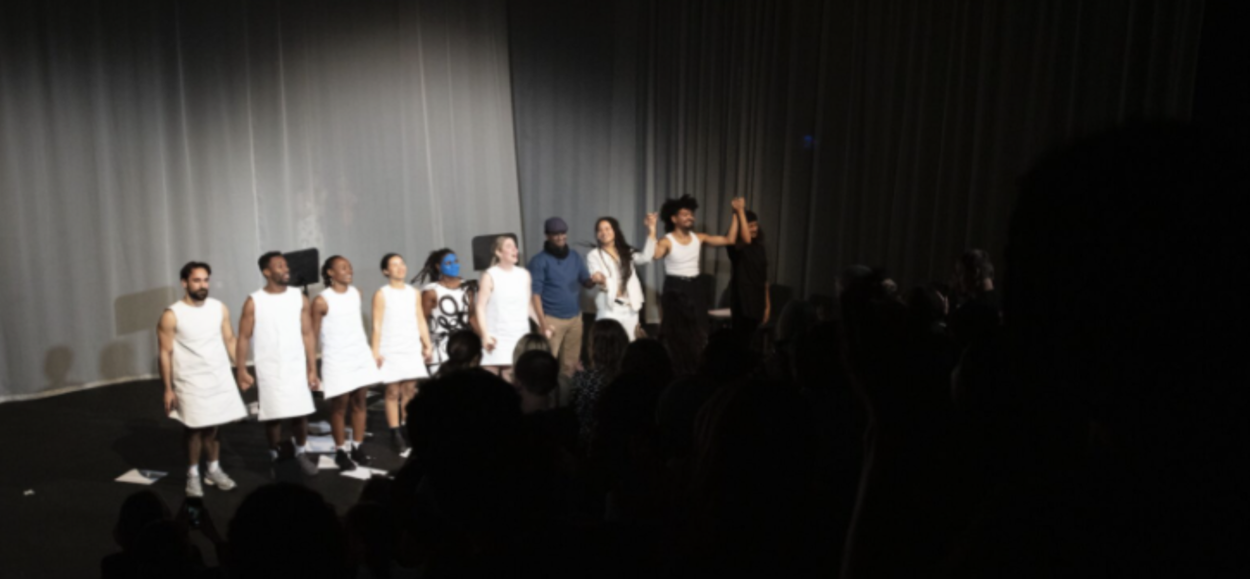 Group of performers taking a bow on stage at the end of a performance, with an audience watching.