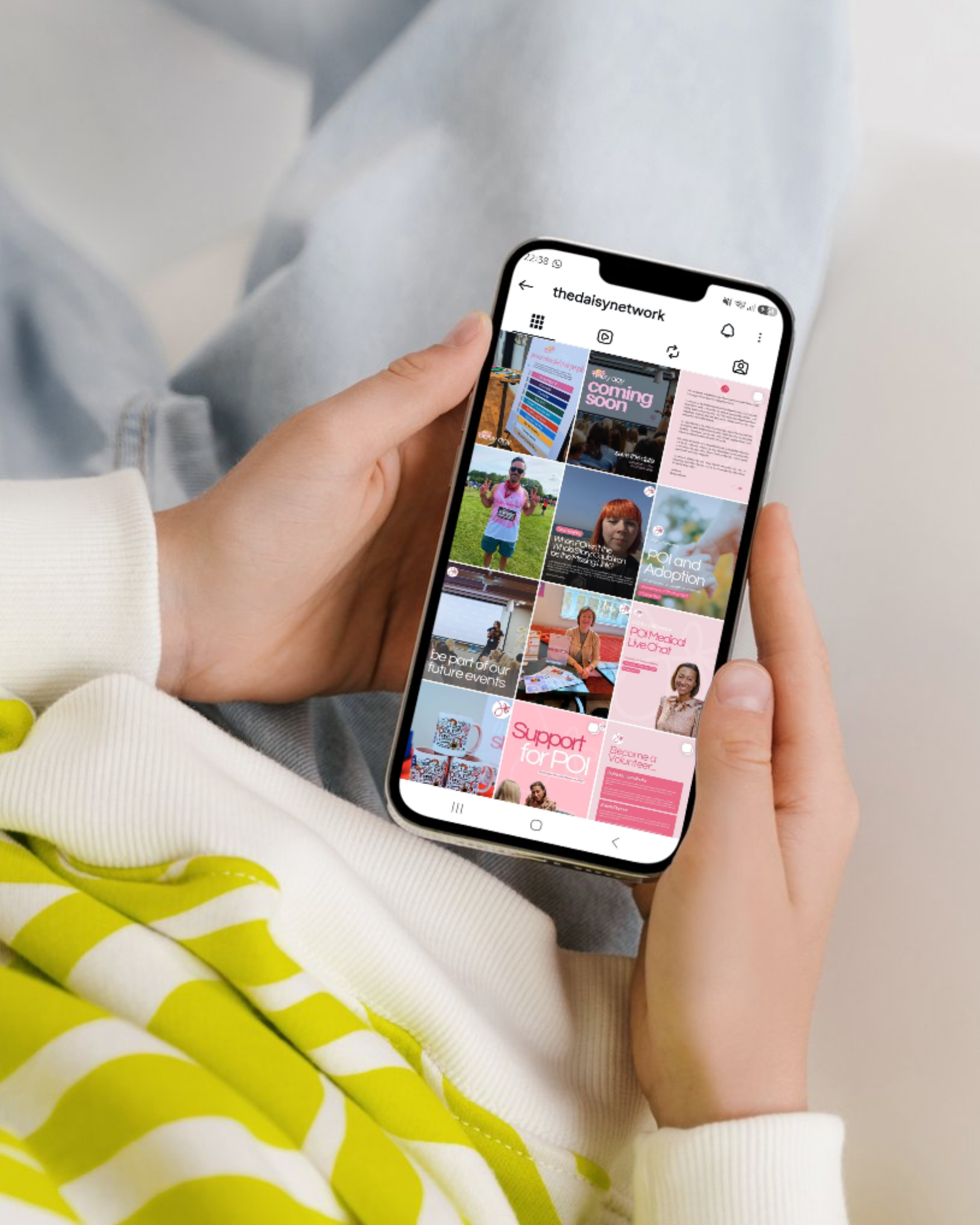 Person holding a smartphone displaying an Instagram profile with various posts, with yellow and white striped fabric in the foreground and light-colored clothing.