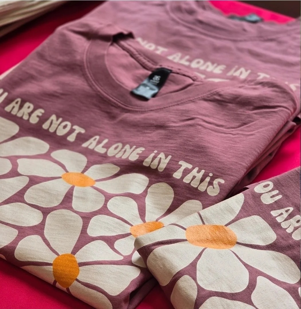 Pink T-shirt with white and orange daisy flower design and printed text.