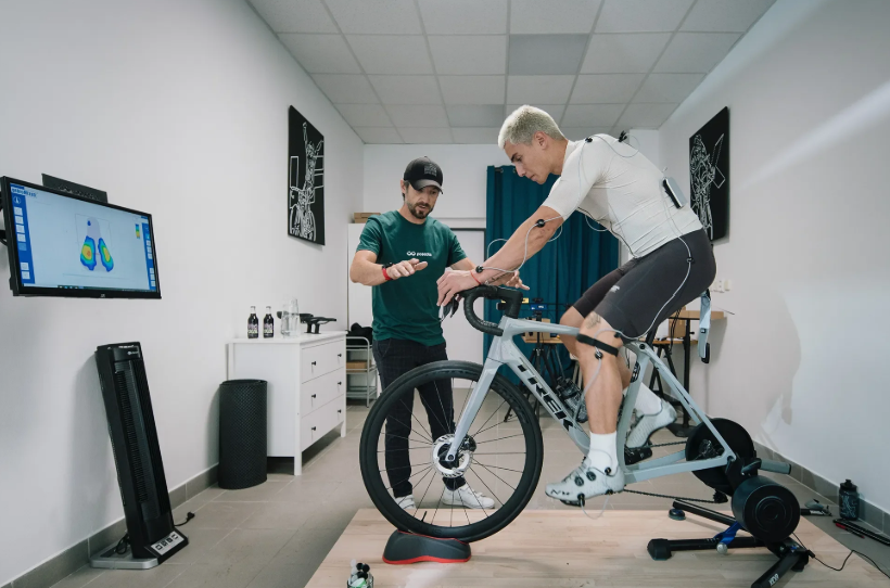 A man on a stationary bike undergoing a clinical gait analysis while a technician records data and monitors the performance.