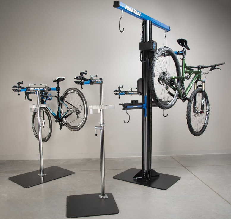 Indoor bike repair stand with three bicycles, one on a black repair stand and two mounted on a vertical bike lift.