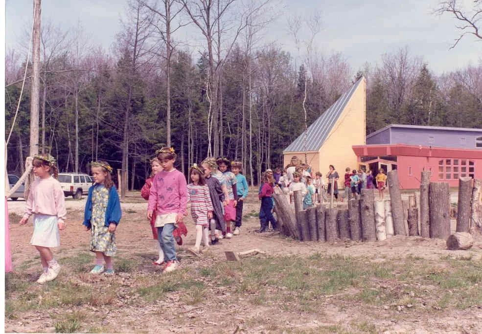 Children participating in outdoor activities at a park or playground with trees and a colorful building in the background.