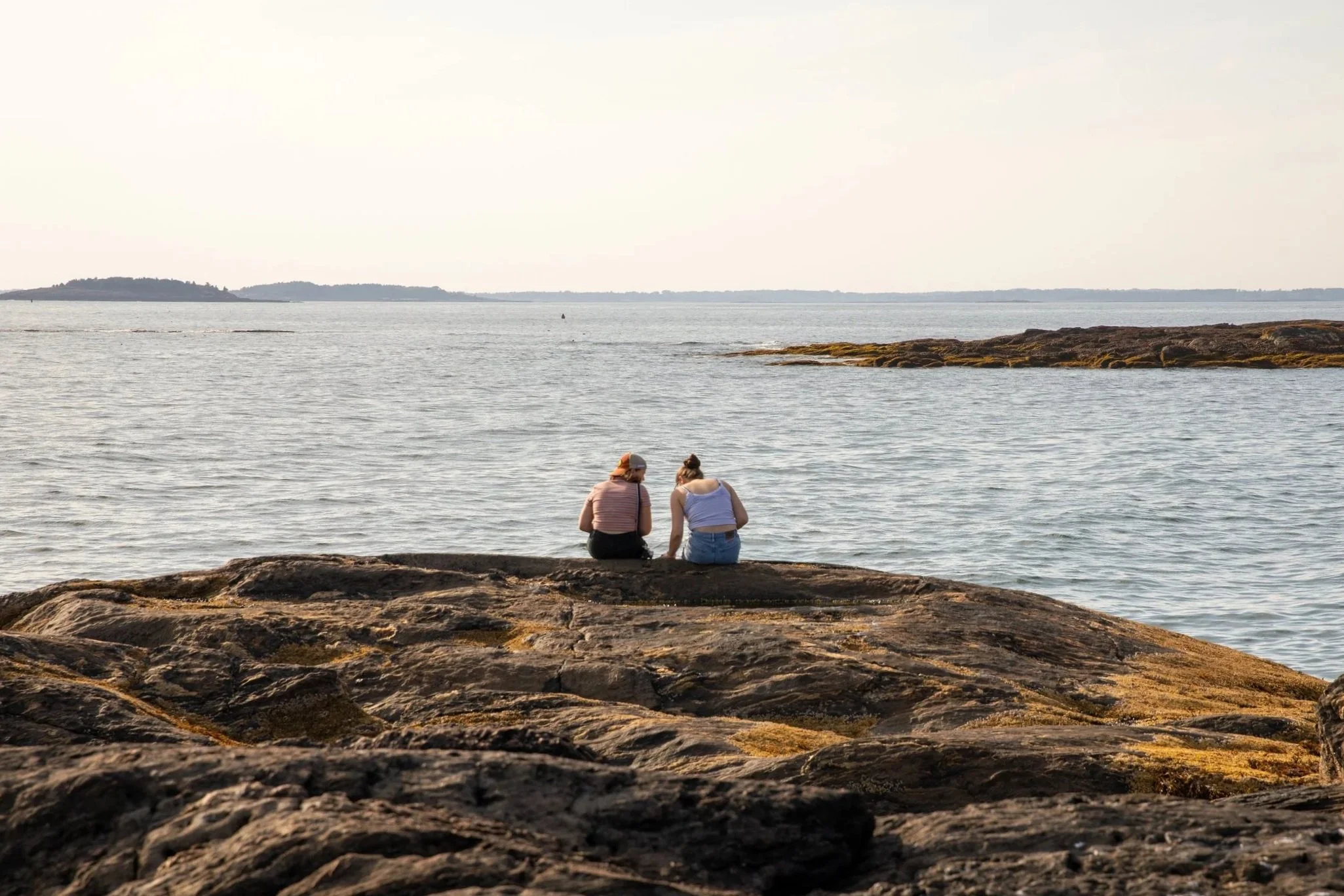 Two high school students sitting on the coast looking out at the water