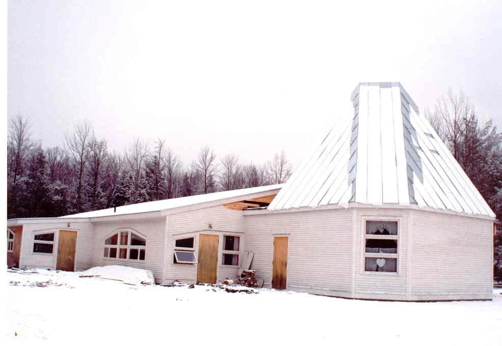 A building under construction with a distinctive rounded tower, snow on the ground, and trees in the background.