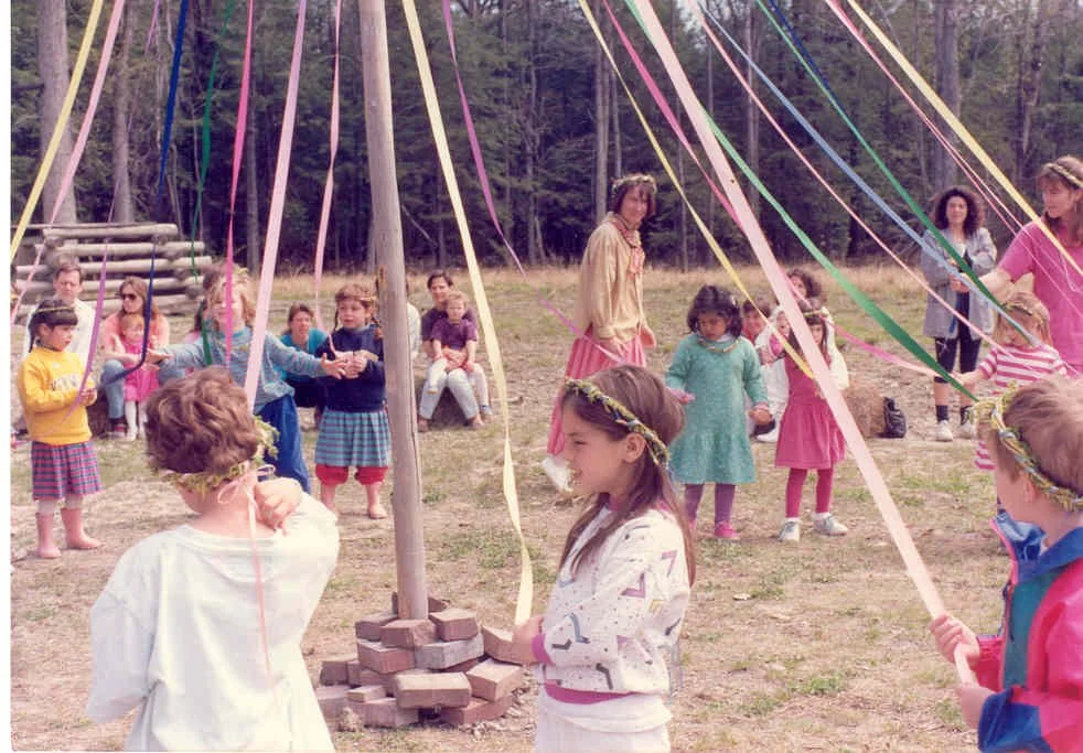 Children participating in a maypole dance at an outdoor gathering.