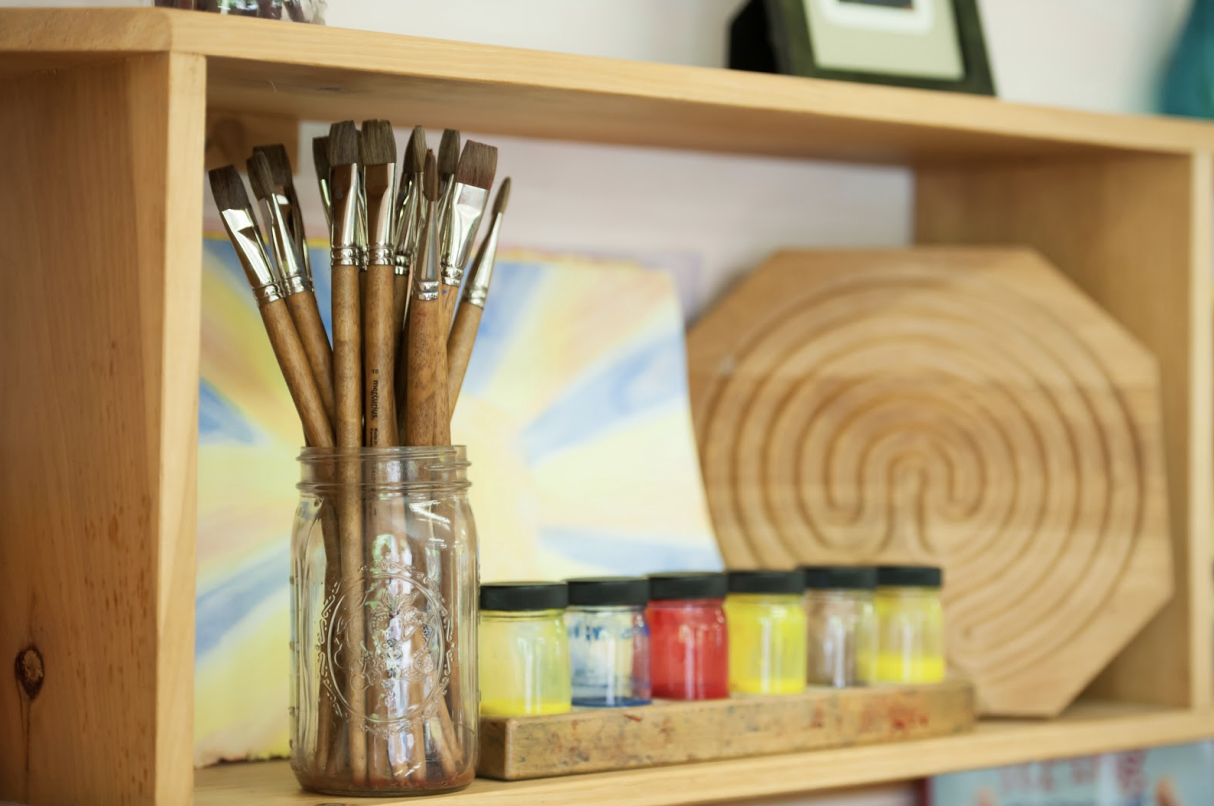 Jar of paintbrushes on a shelf next to paints