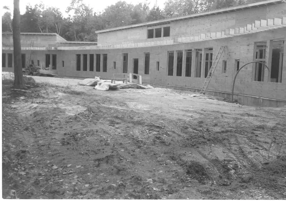 Construction site with a large, partially built building, ladders, and construction materials on uneven ground.