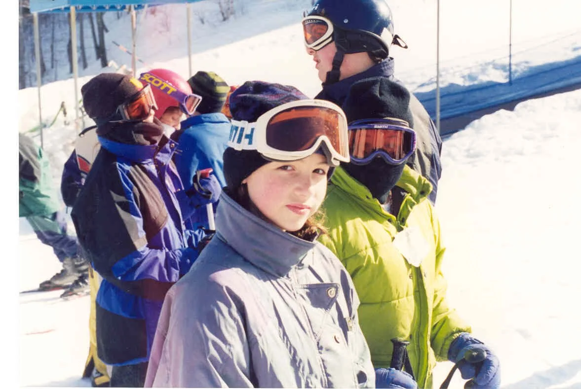 Group of children and adults in ski gear standing in a line on snowy mountain with ski equipment and safety netting