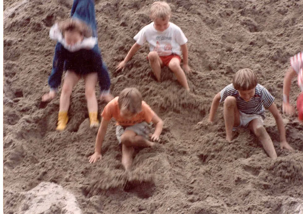Children playing in sand, digging and building holes at the beach or sandbox.