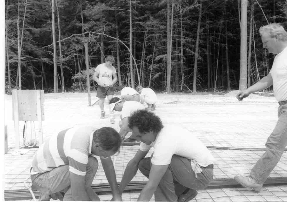 Construction workers and children working on a building site, with trees in the background.