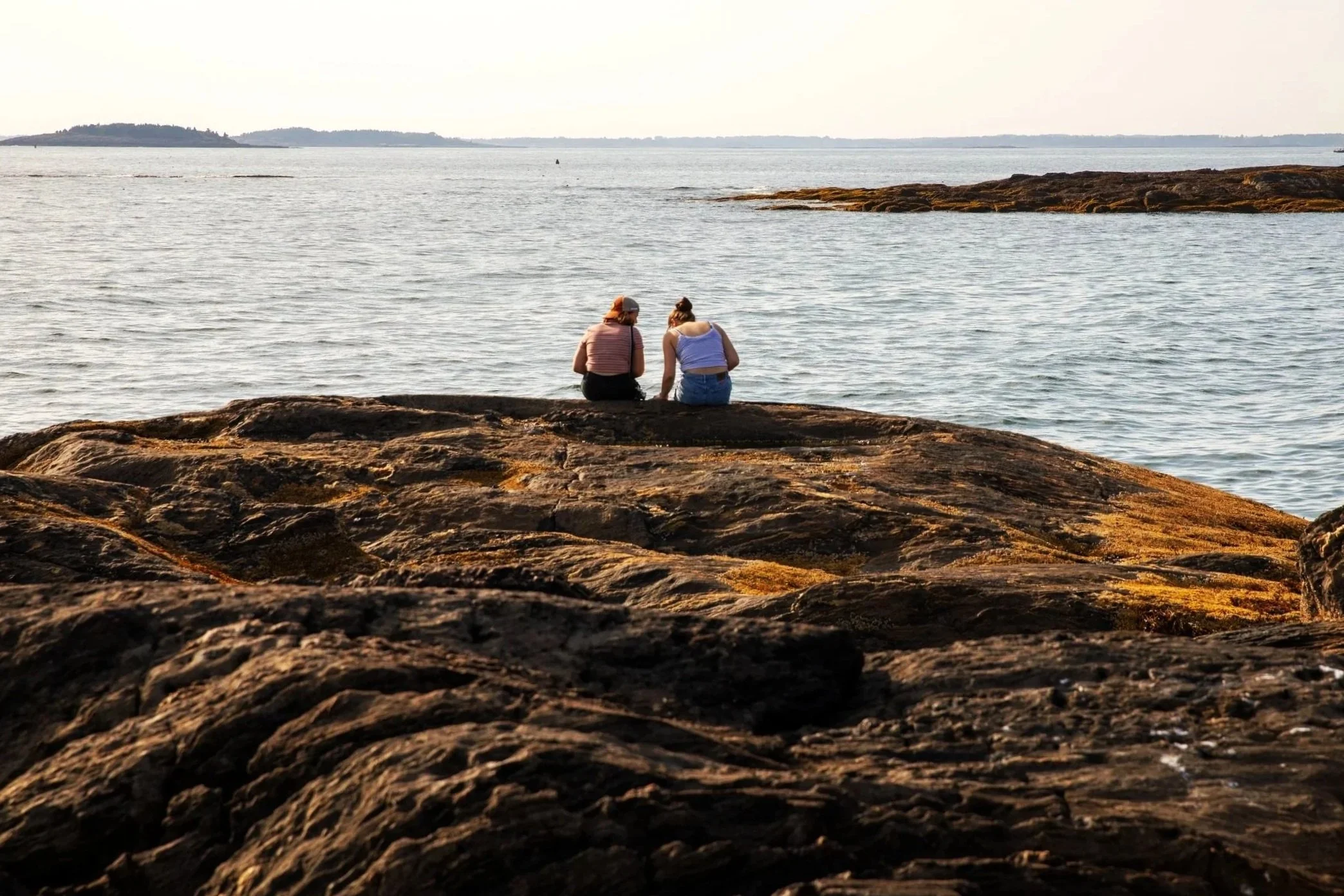 Two high school students sitting on the shore looking at the ocean