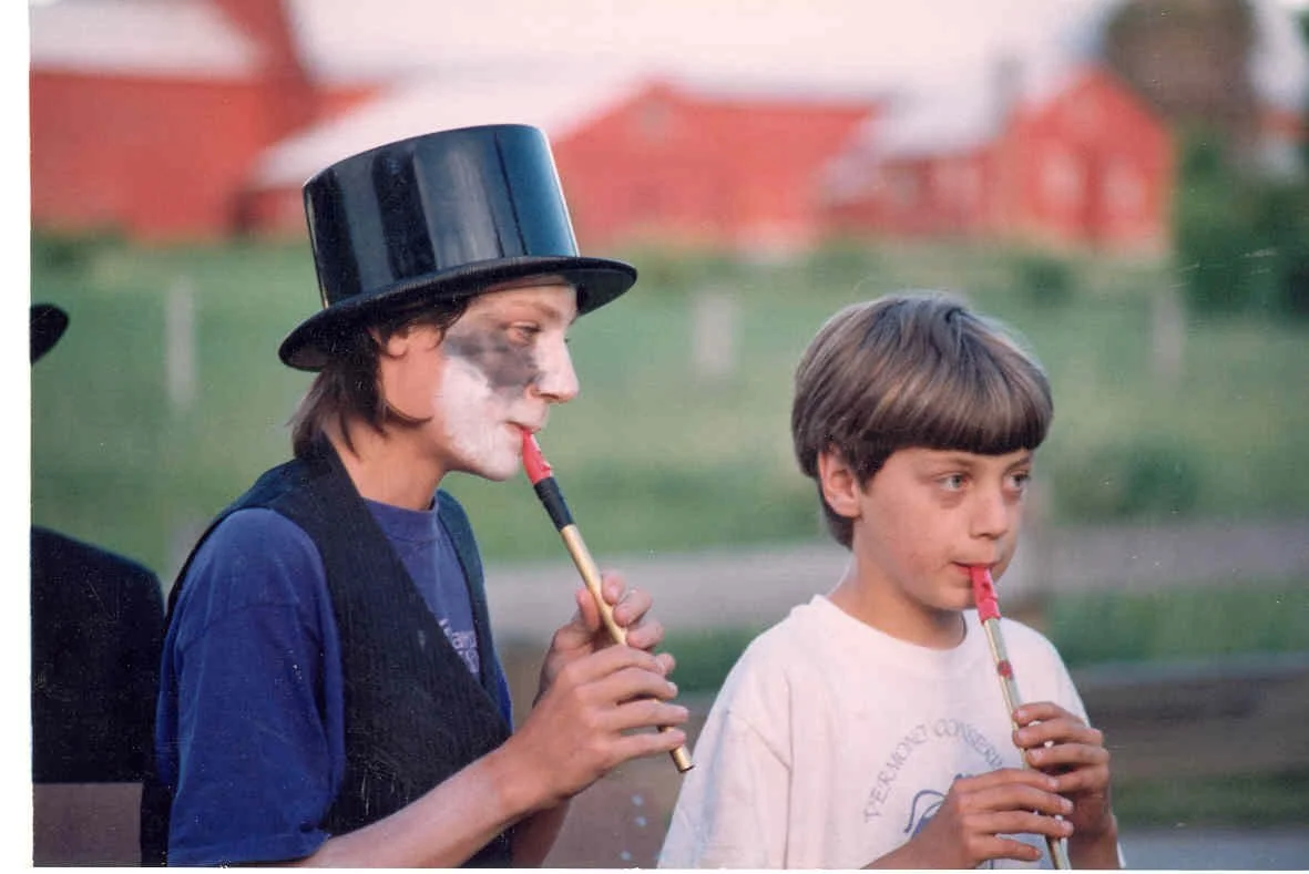 Two young boys playing recorders, with one boy wearing a top hat and face paint.