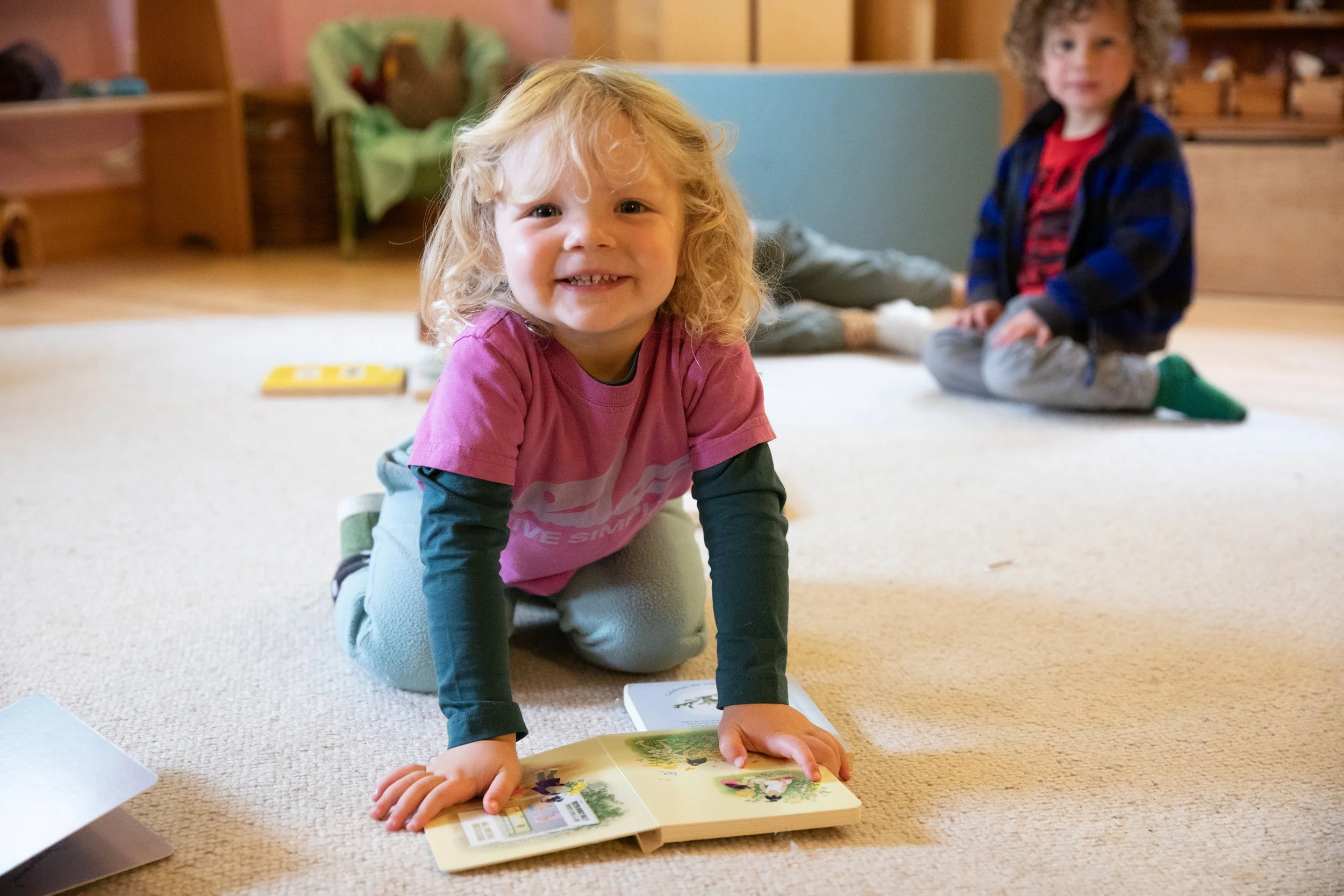 Toddler smiling while reading on a carpet