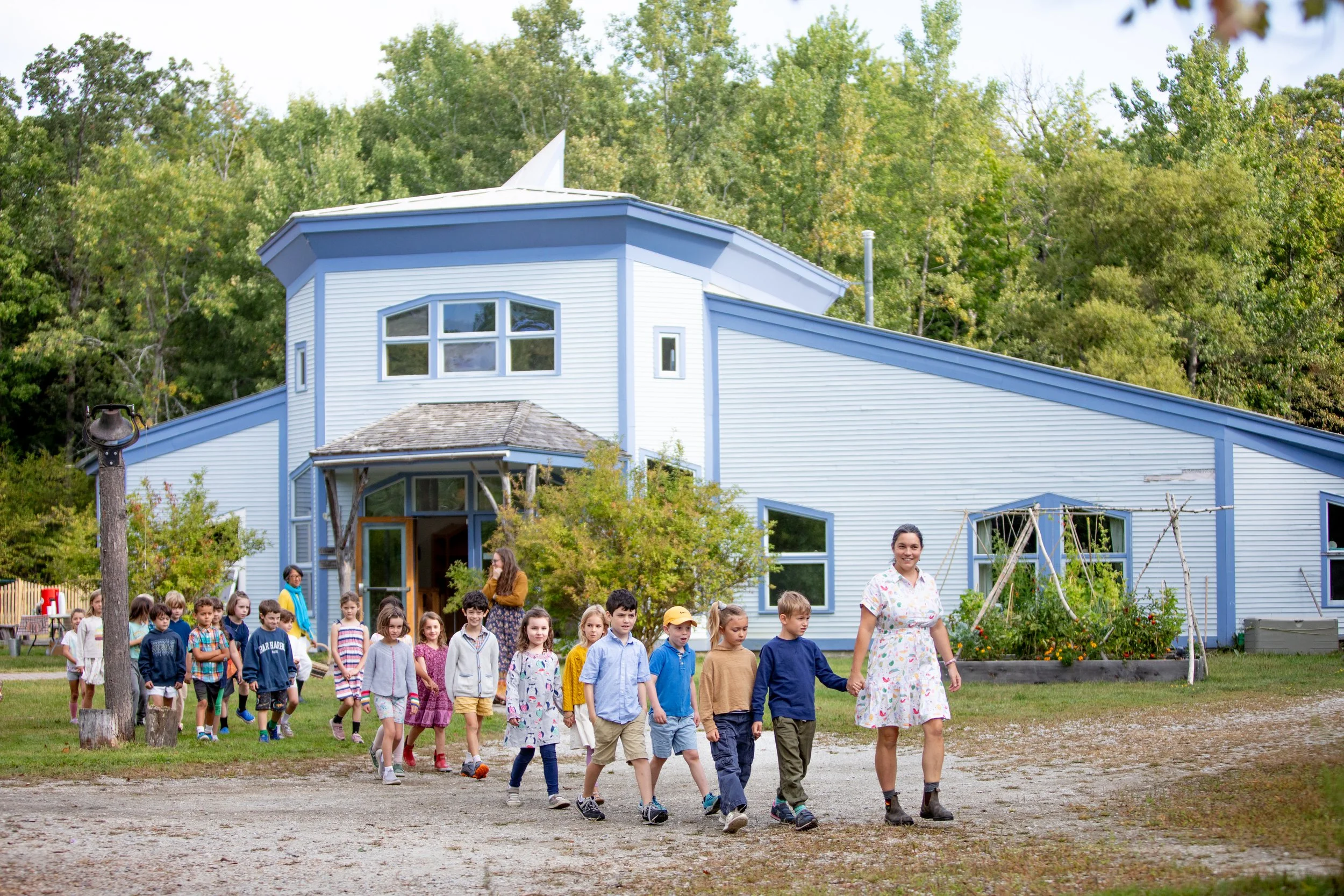 Teacher leading grade school students outside with their school in the background