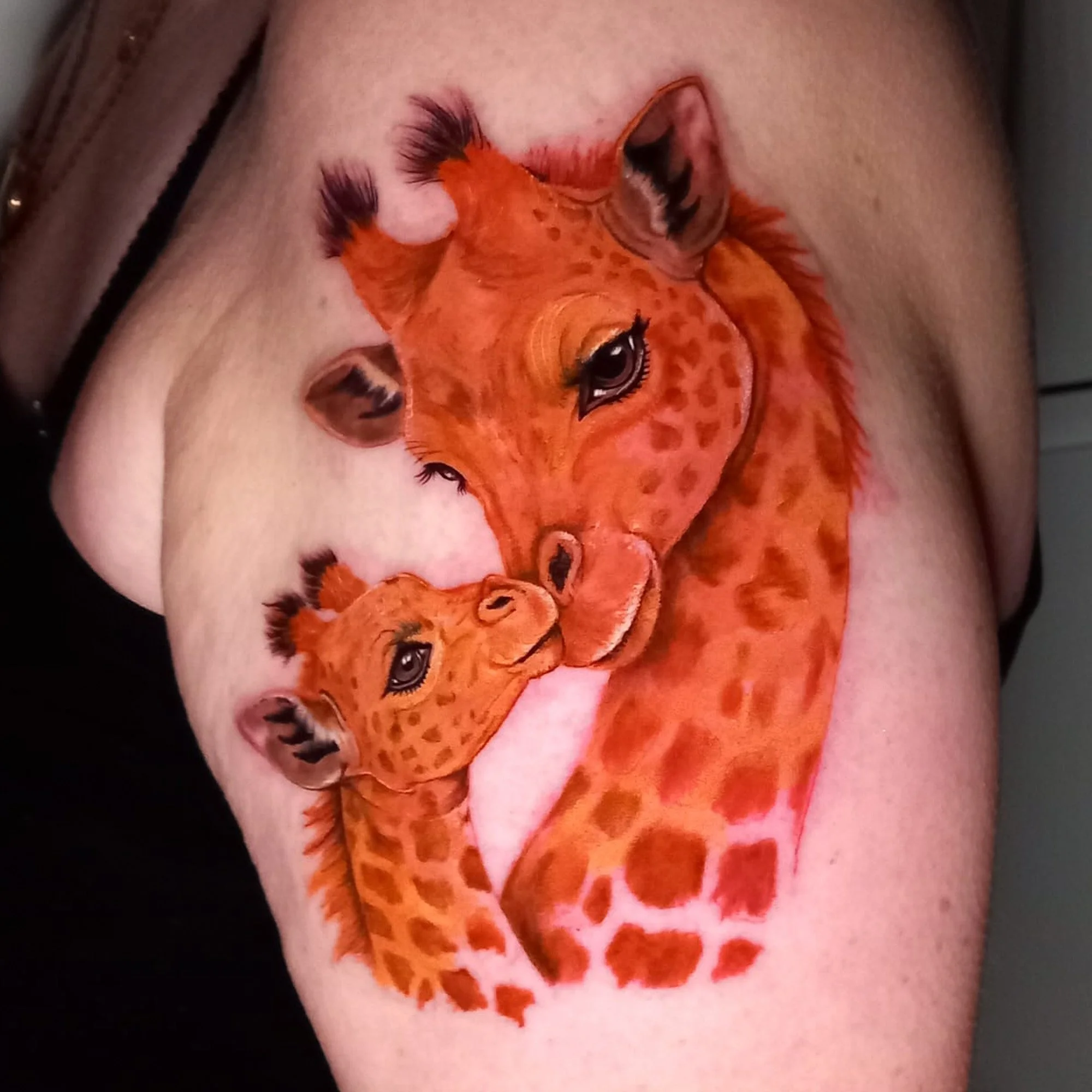 A close-up of a tattoo of a realistic orange giraffe adorned with detailed features and eyelashes, on a person's skin.