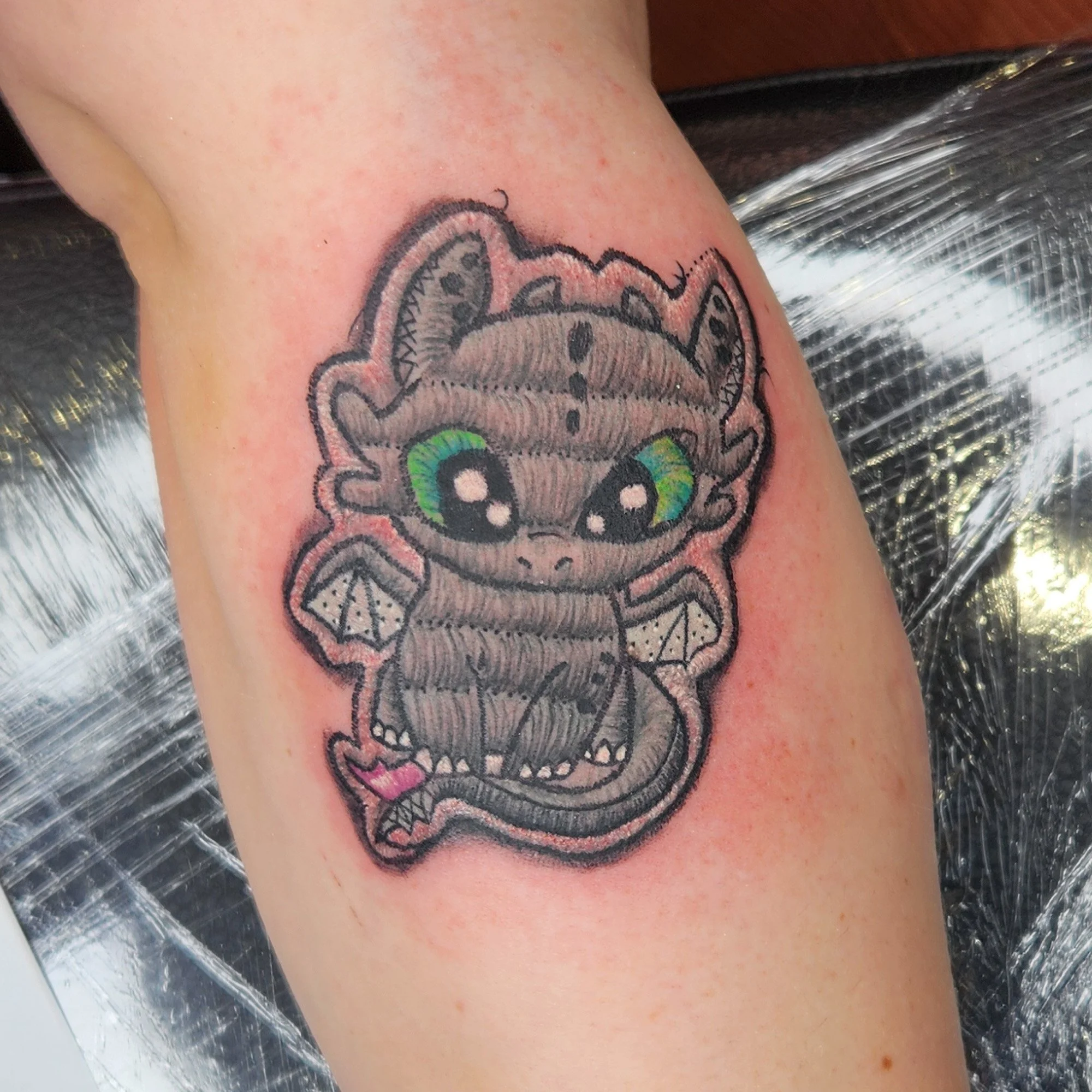 Close-up of a person's skin with a tattoo of a cartoonish dragon.